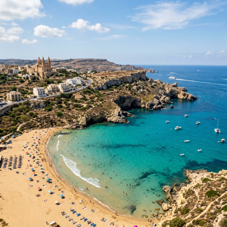 Turquoise bay with sandy beach, swimmers, boats, and a large church on a hill