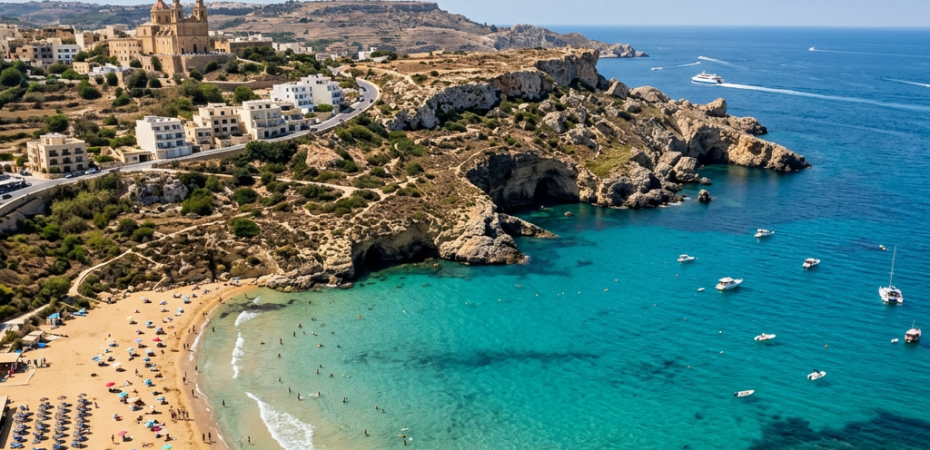 Turquoise bay with sandy beach, swimmers, boats, and a large church on a hill